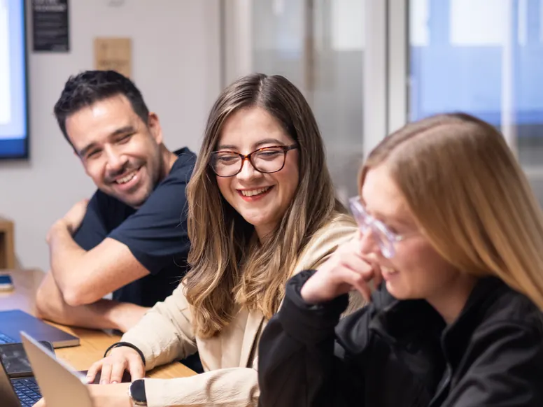 Three ClearCalcs team members laughing over their laptops in the Bogota office