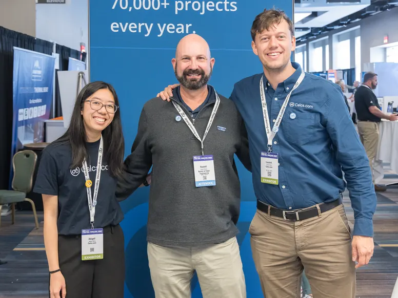Two Calcs.com team members with an attendee in front of a stand banner reading 70,000+ projects every year