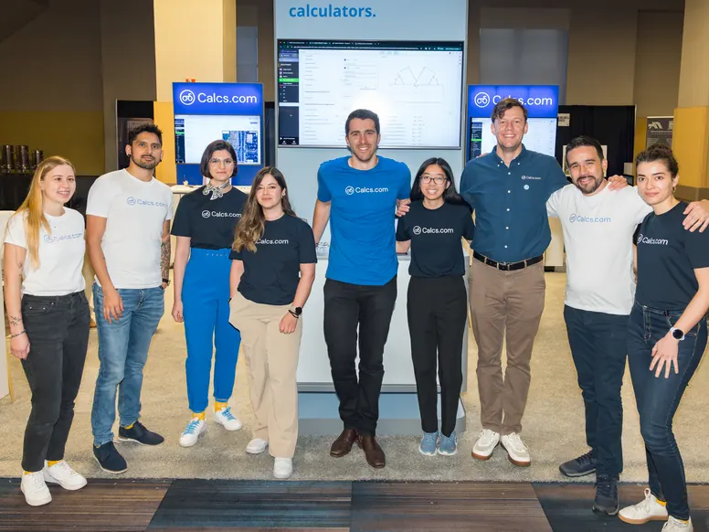 Nine Calcs.com team members lined up in front of the stand screens